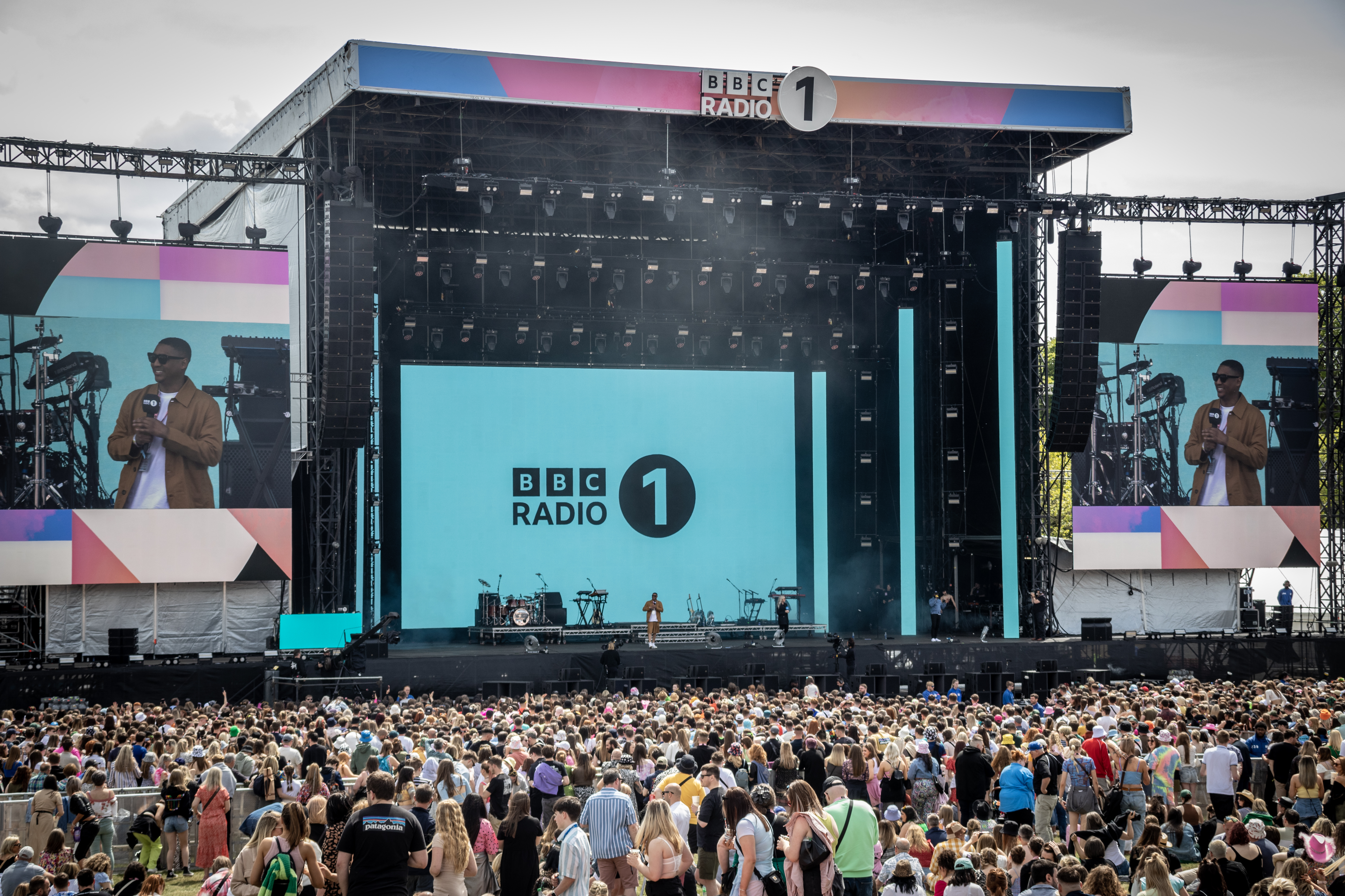 A stage with people around it. It is branded in blue and pink with BBC Radio 1 written on it.