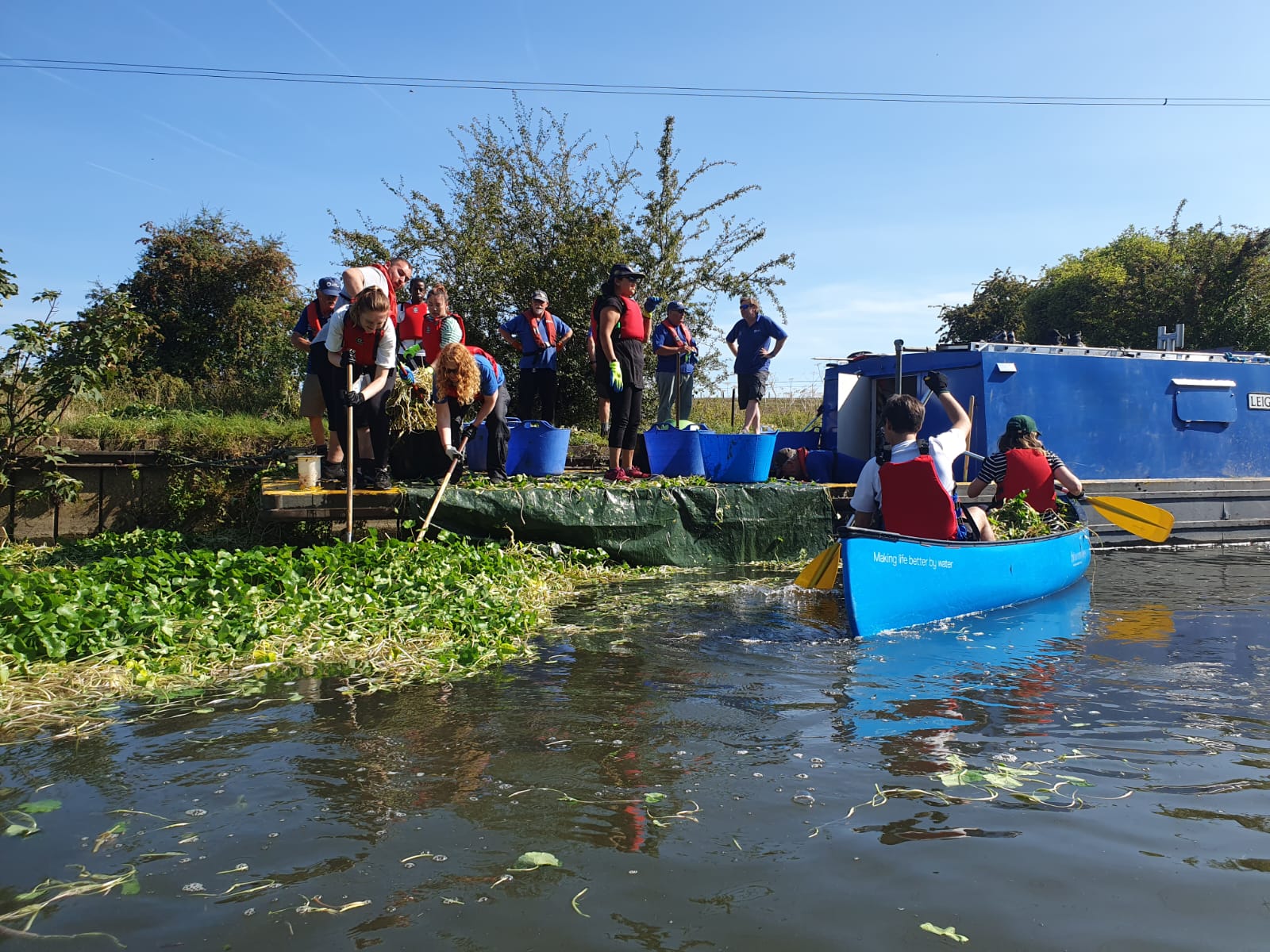A group of people canoe down a river whilst cleaning it up of rubbish and litter.