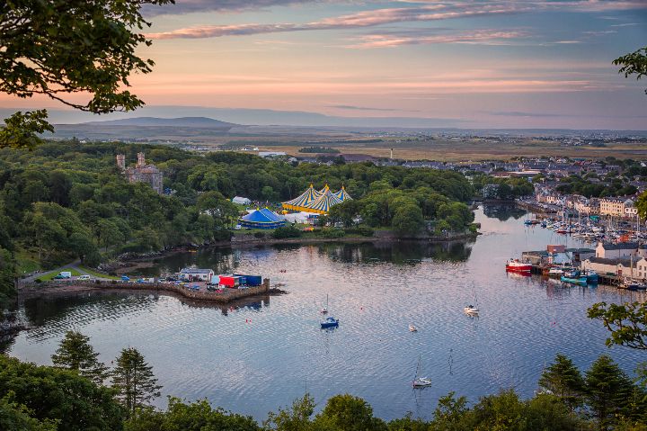 A view of a lake with tents dotted around it - with boats resting on the calm water.