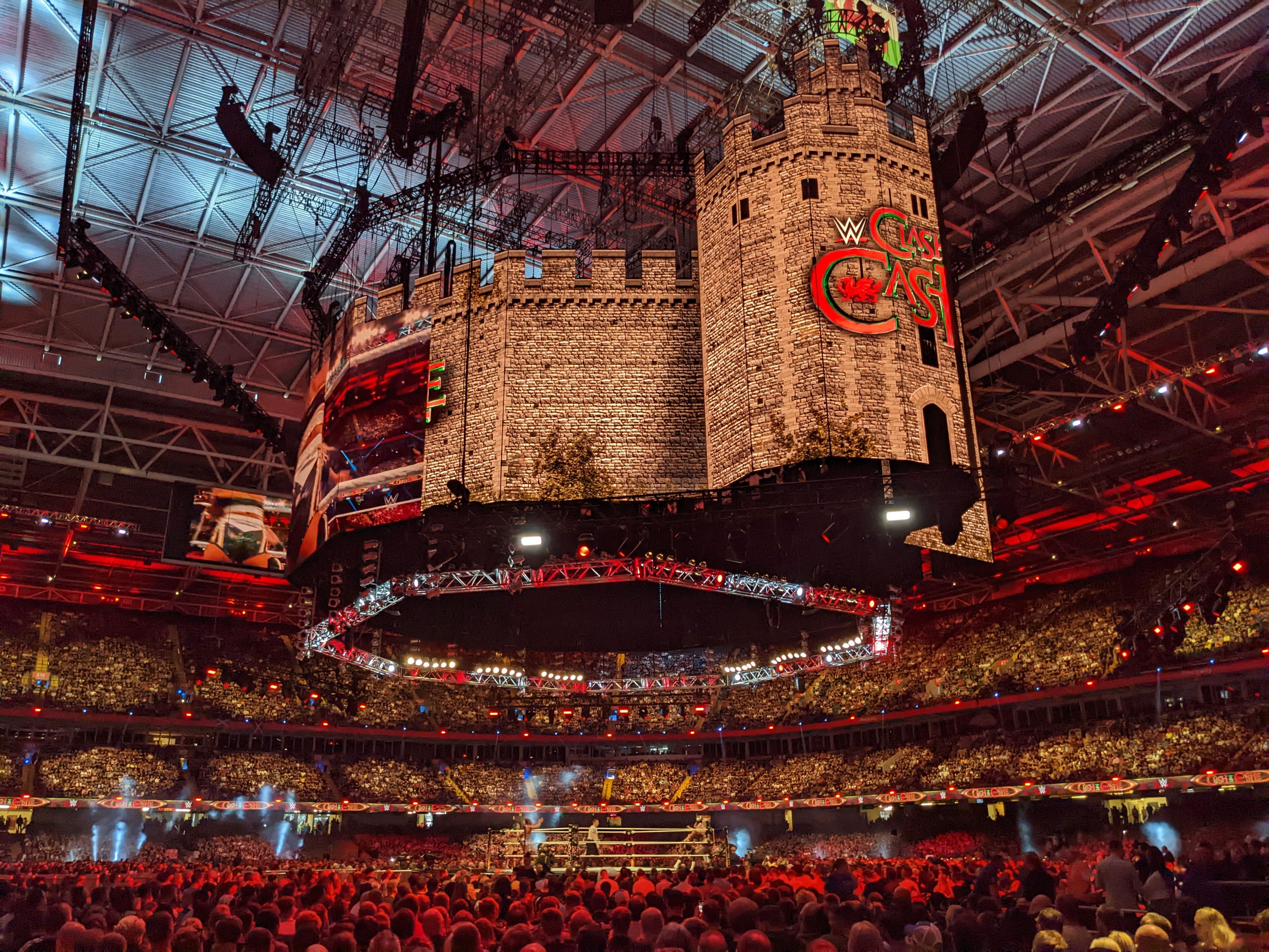 An inflatable castle hangs from the ceiling of a stadium full of fans with a ring in the middle.