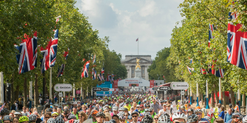 The Mall in London is full of people with Buckingham Palace in the background, union jacks are flying.